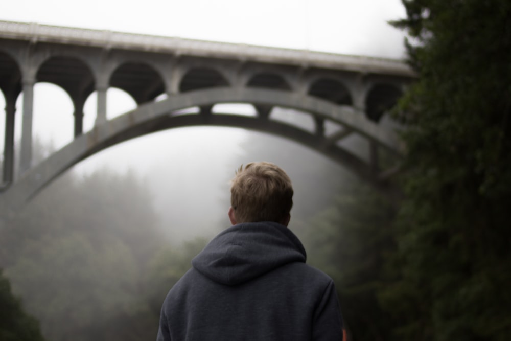selective focus photo of man standing infront of bridge