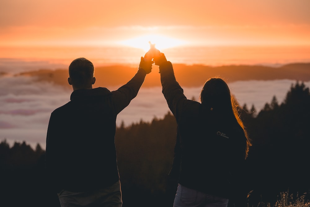 silhouette of woman and man holding hands facing sea of clouds during sunset