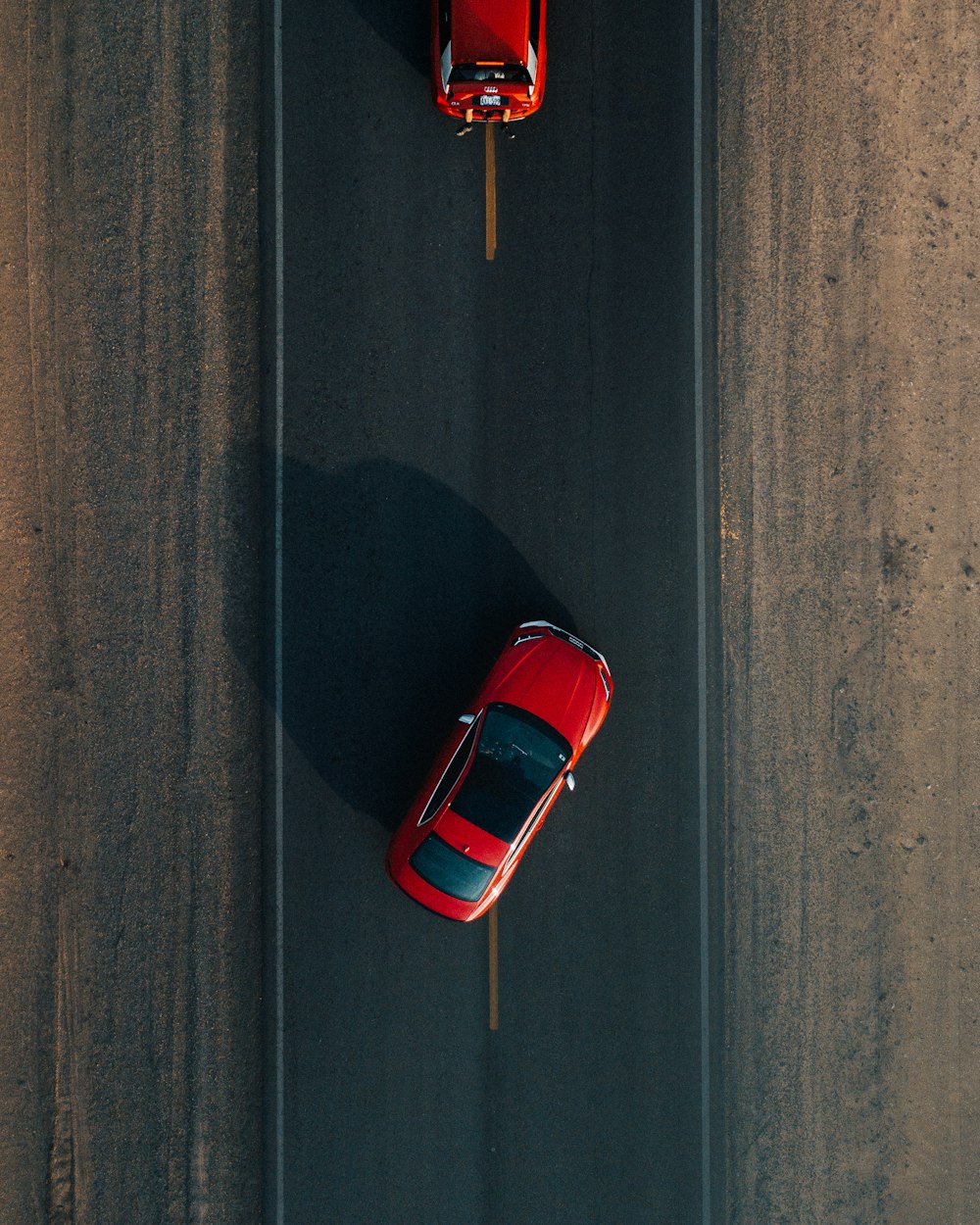 昼間、道路を走る赤い車2台