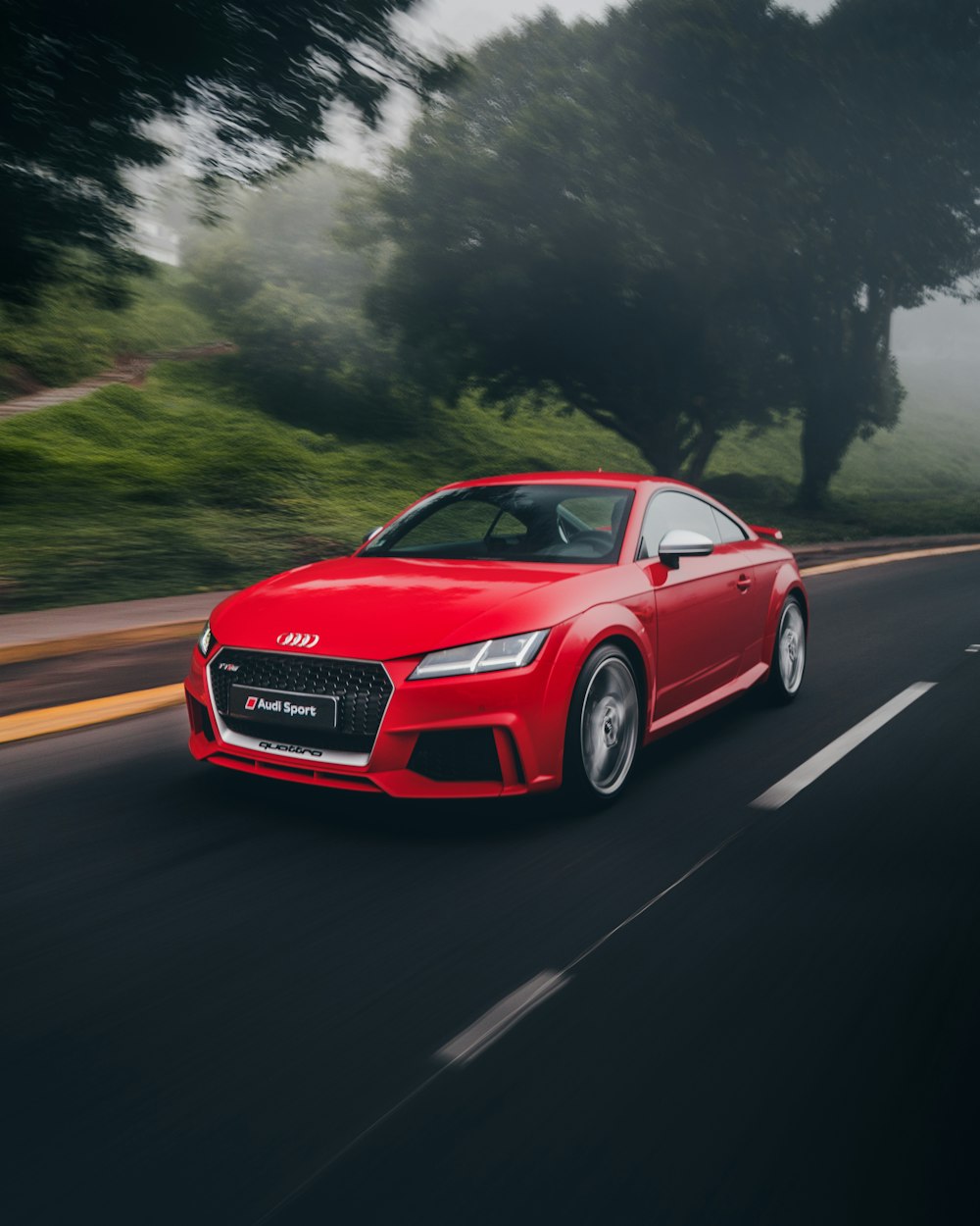 cupê Audi vermelho na estrada perto de árvores durante o dia