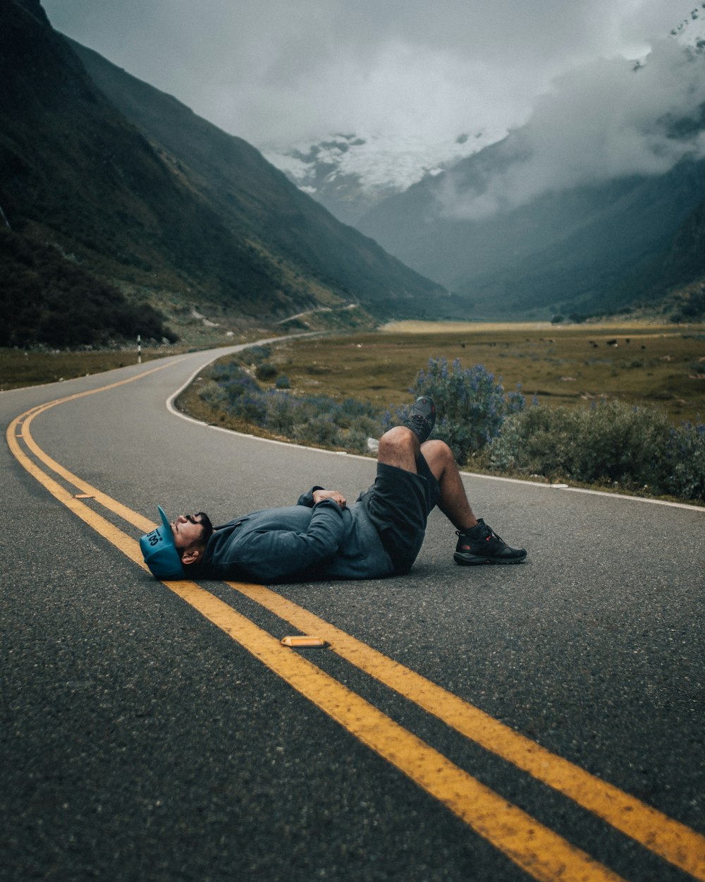 緑の葉の植物の近くの黒いコンクリートの上の道路に横たわる男