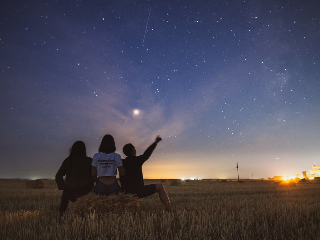 three people looking and pointing at stars while sitting on a bail of hay