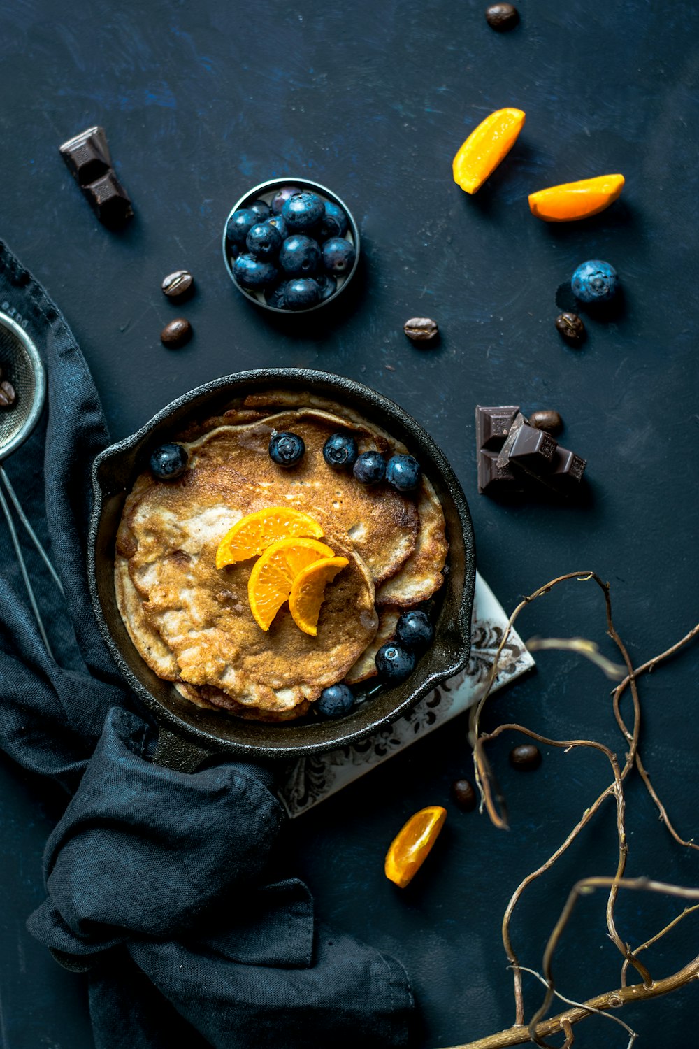 Pancake con arancia e mirtilli accanto a cioccolato sparso e chicchi di caffè