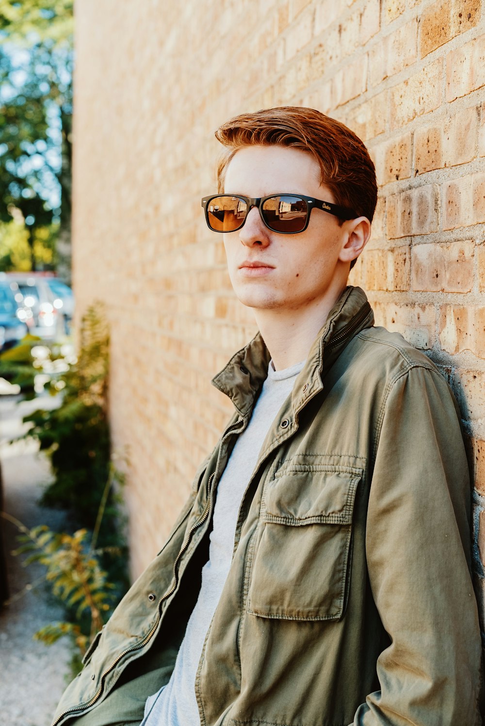 man in green jacket leaning on brown brick wall