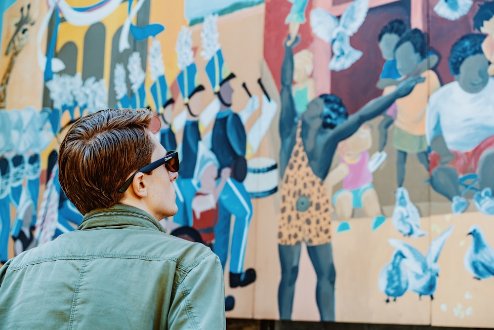 man in green collared top staring at graffiti wall