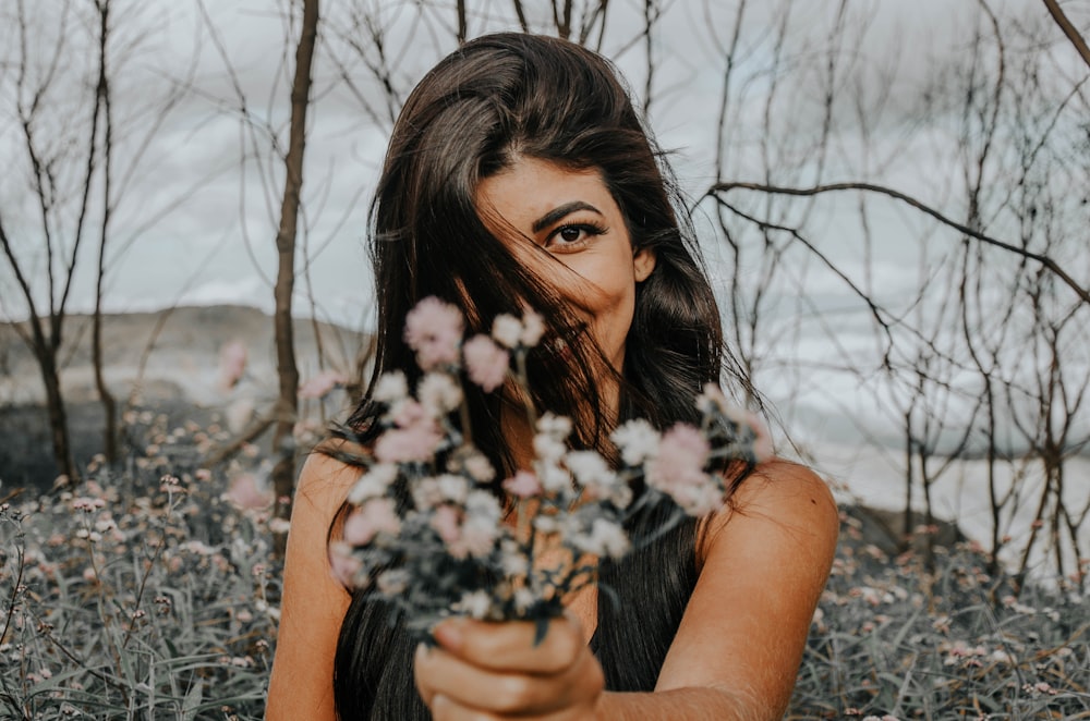 mujer sosteniendo flores blancas rodeada de árboles desnudos