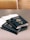 Five dark blue passports from the United States of America are placed on a gray table. Each passport displays the country's emblem and name in gold lettering. In the background, there is a chair with a circular patterned fabric.