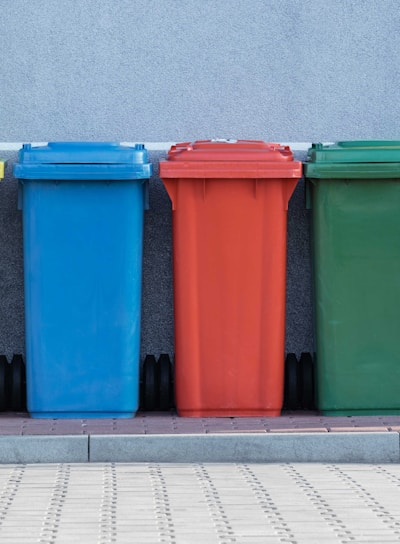 four assorted-color trash bins beside gray wall