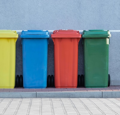 four assorted-color trash bins beside gray wall