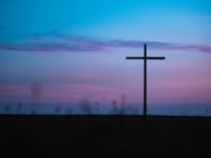 A peaceful outdoor scene with a cross silhouetted against the sky.