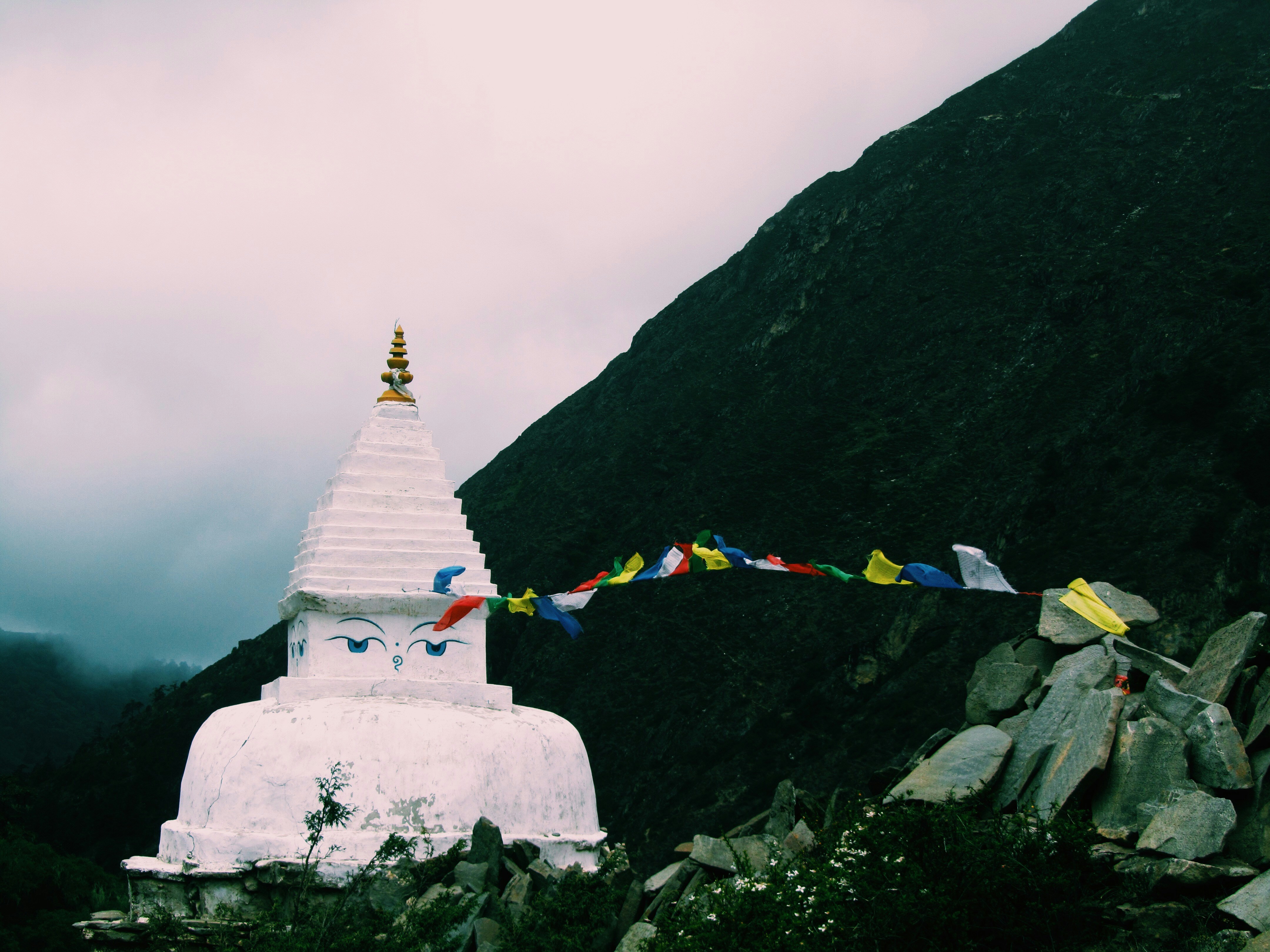 white concrete temple near mountain under white sky, On our way back, the sky turned grey, the wind started to hit and I saw this beautiful sight.
