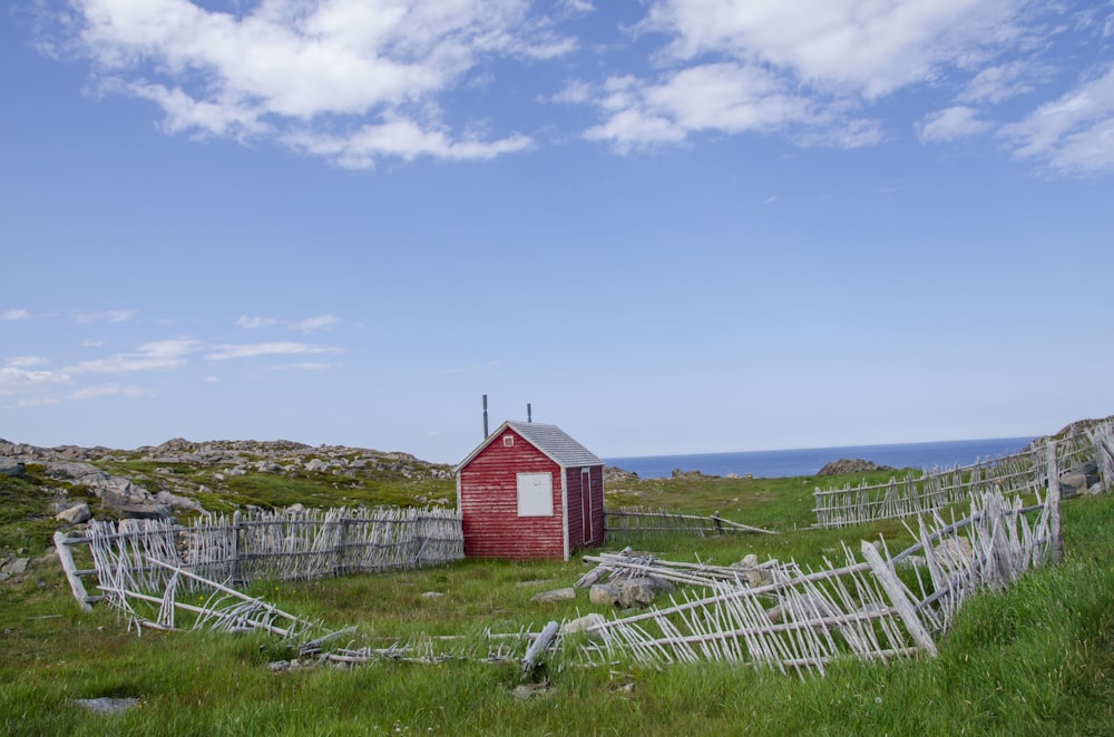 red shed with wrecked fences under blue sky and white clouds during daytime