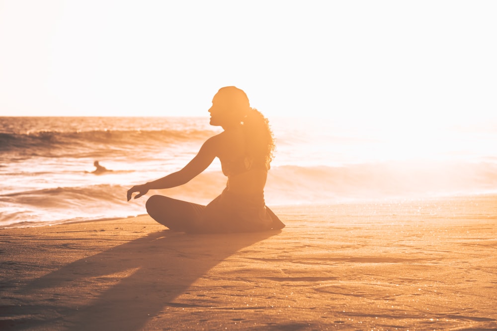 Silhouette einer Frau, die während des Sonnenuntergangs am Meeresufer sitzt