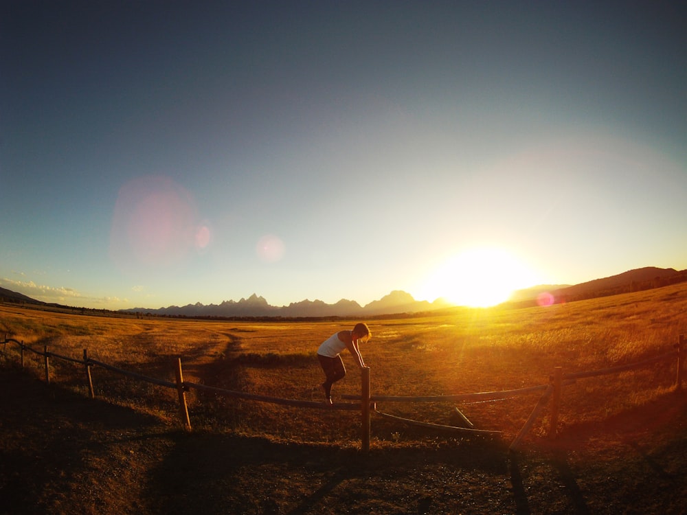 person standing on wooden fence during sunset