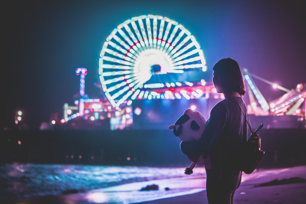 woman standing on shore near themed park during night