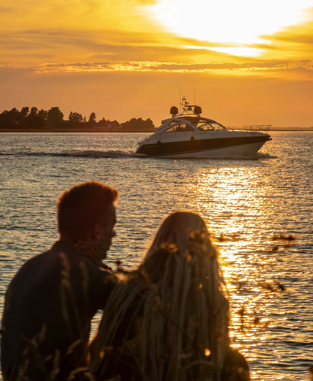 man and woman watching sunset by the sea with view of cabin cruiser