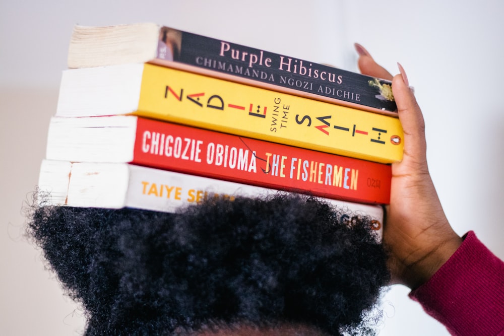 person carrying four assorted-title books on head