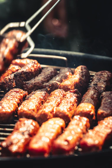 Close-up of a juicy grilled chorizo sizzling on the barbecue with herbs sprinkled on top.