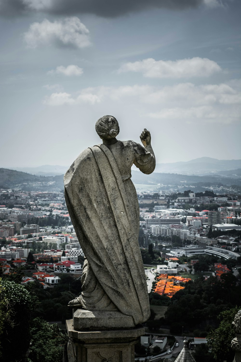 woman statue near village and mountain range under cumulus clouds