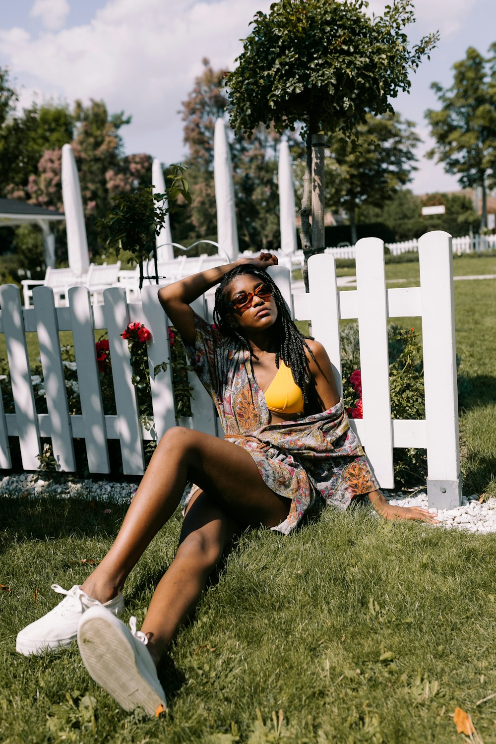 woman sitting on grass while leaning on white fence