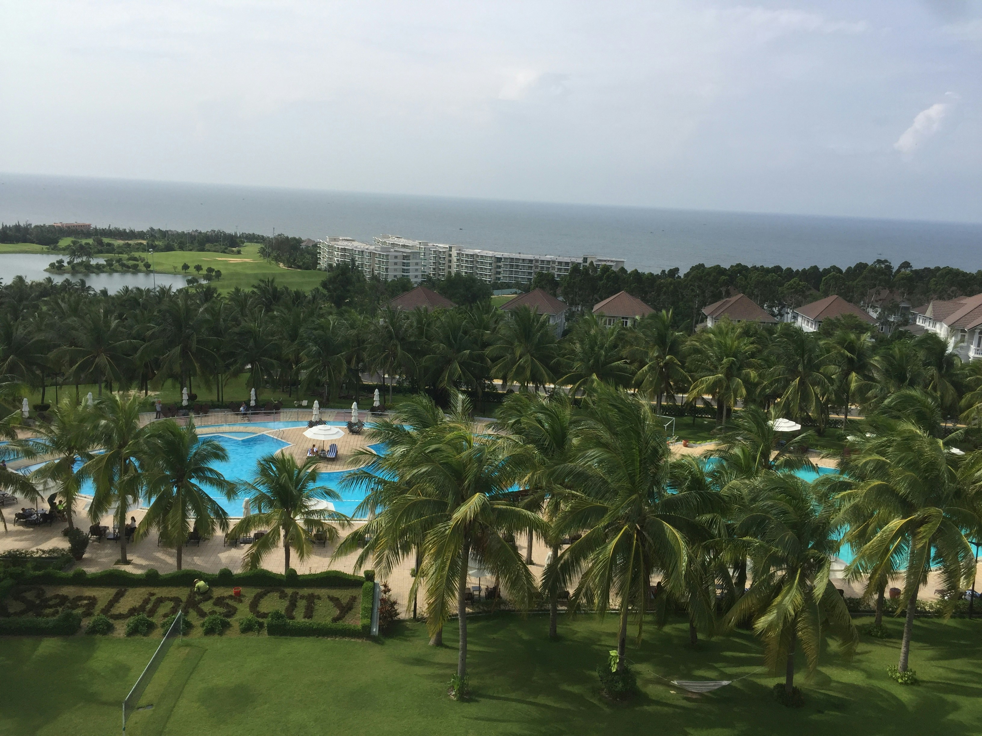 Resort-style swimming pool surrounded by palm trees and landscaped gardens, bright airy setting