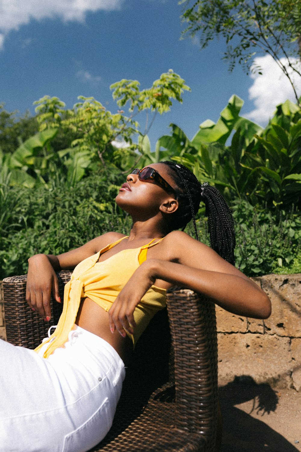 a woman in a yellow shirt and white pants sitting on a wicker chair