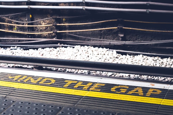 the words "mind the gap" over a yellow line against the rail of a train track