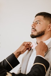 A well-dressed man adjusting his tie in front of a mirror.