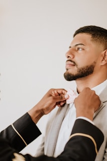 A groom adjusting his bow tie in front of a mirror.
