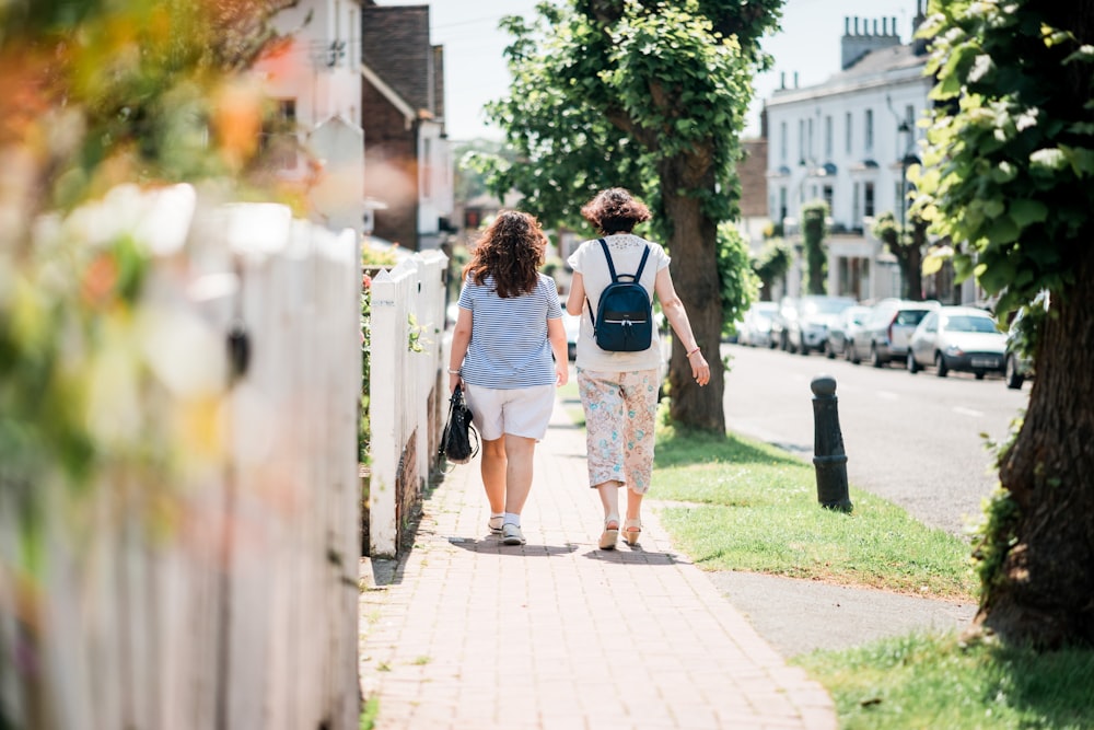 two women walking down sidewalk near fence