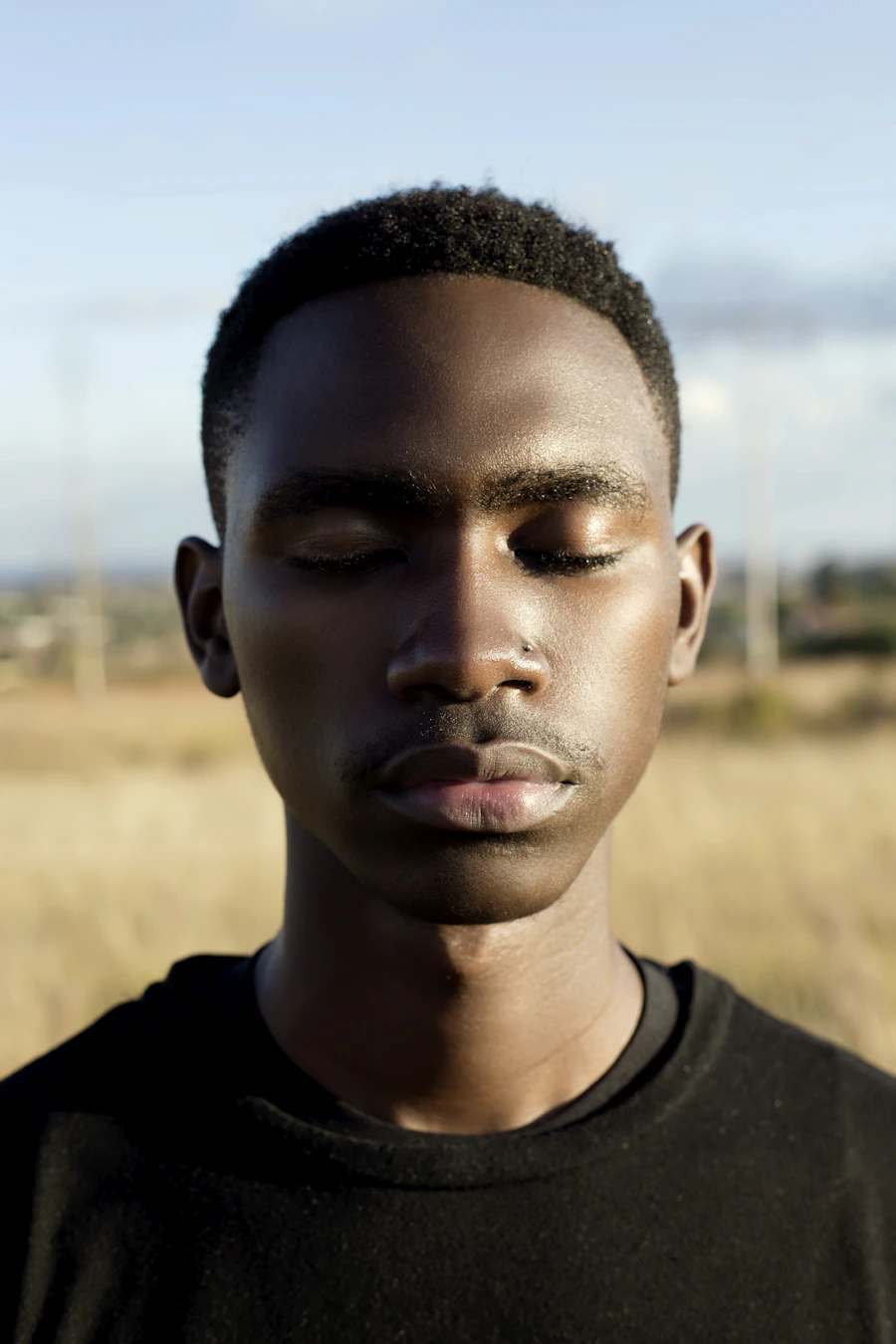 An adult stands outdoors with eyes gently closed, taking a slow steadying breath in warm golden light