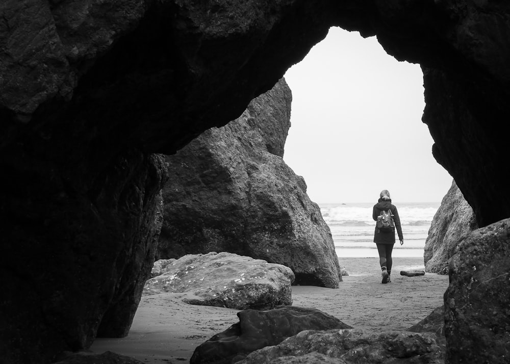 person walking beside rock formation near cave