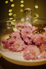 Pink flowers are artfully arranged under a glass dome with soft, golden bokeh lights in the background creating a warm and inviting ambiance.