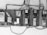 A row of old electric meters mounted on a wooden board are connected by various electrical wires. Some of the meters are encased, while others have exposed switches and dials. The setup appears rustic and utilitarian, with cables running horizontally and vertically.