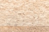 A textured surface composed of wood chips and strands oriented randomly and pressed together. The material appears natural and rustic, with variations in the shades of brown, beige, and tan.