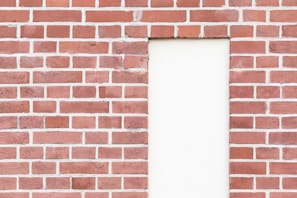 A red brick wall with an inset rectangular section filled with plain white plaster. The bricks are neatly arranged in a classic pattern with visible mortar lines.