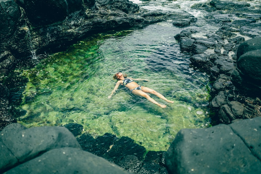 mujer flotando en un cuerpo de agua rodeado de piedras