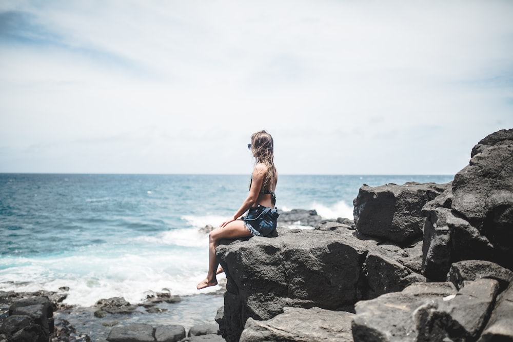 woman sitting on edge of rocks near sea