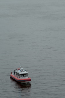 A small boat with red and white colors floats on calm water. The boat appears to have modern equipment and is likely a patrol or rescue vessel.