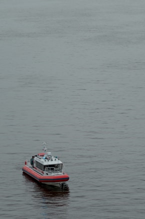A small boat with red and white colors floats on calm water. The boat appears to have modern equipment and is likely a patrol or rescue vessel.