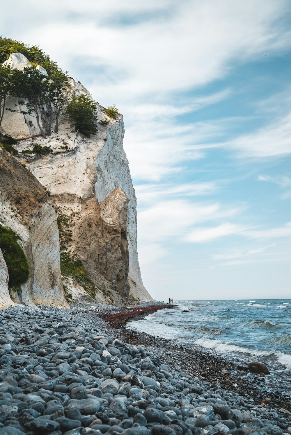 two person standing between cliff and body of water