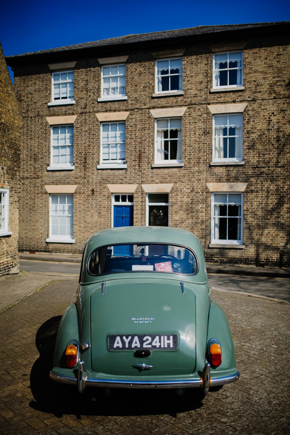 teal Volkswagen Beetle in frotn on brown 3-storey building