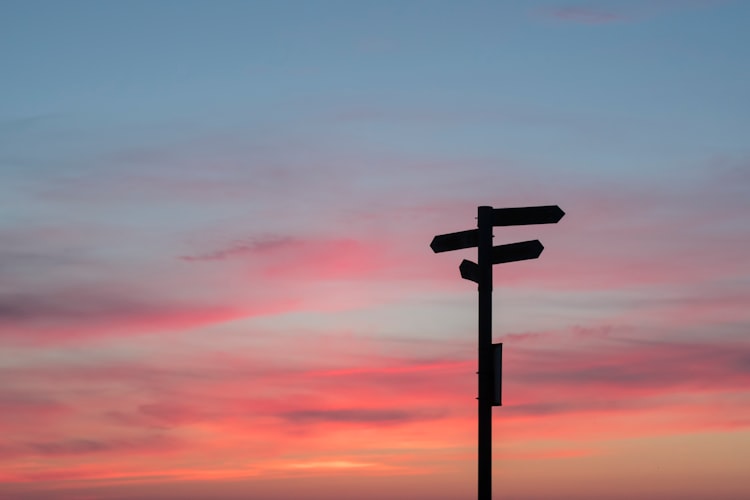 A sunset with the black silhouette of a signpost pointing in several different directions. 