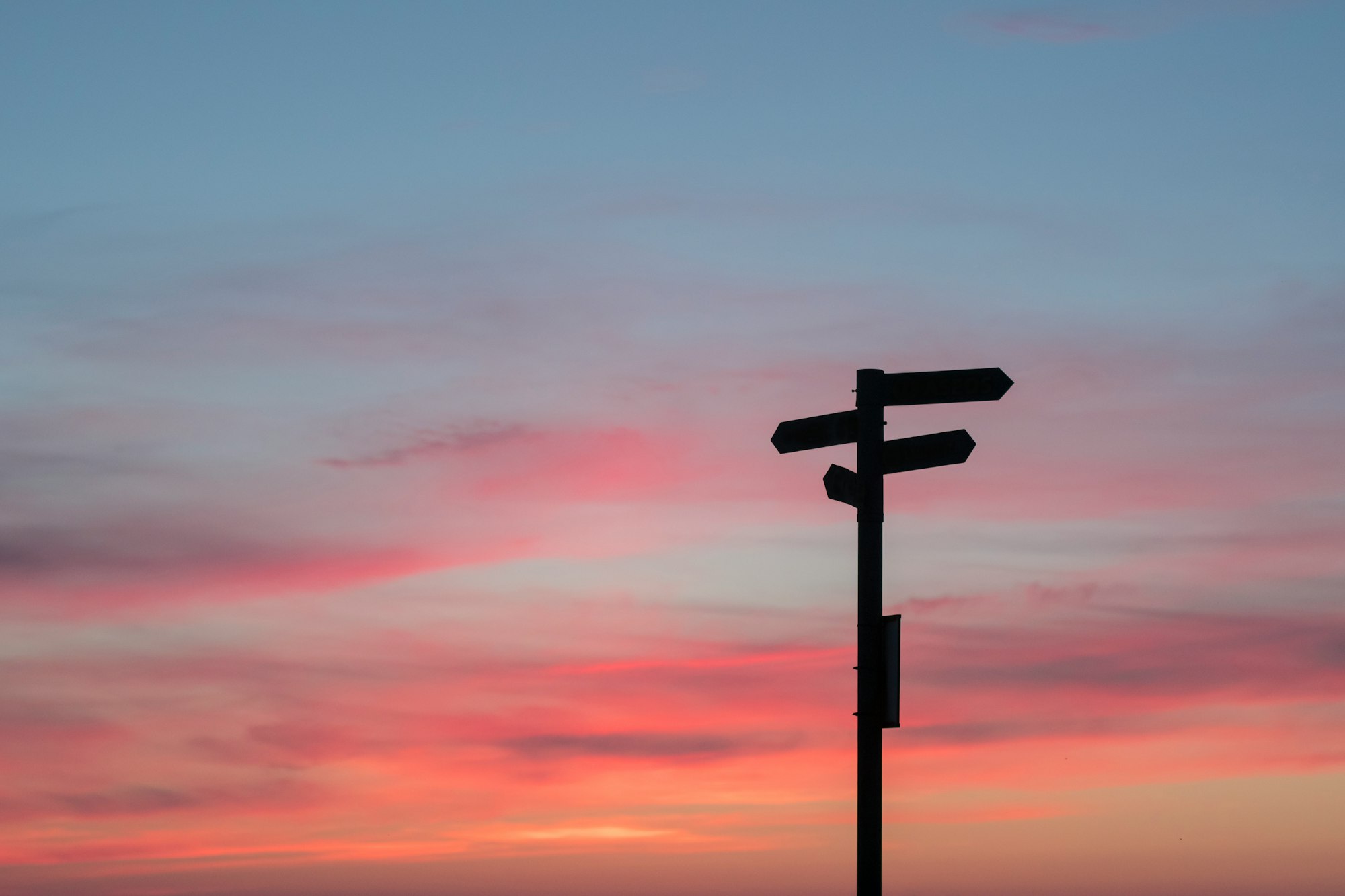 Silhouette of a signpost pointing in many directions, with the sky in sunset colours in the background
