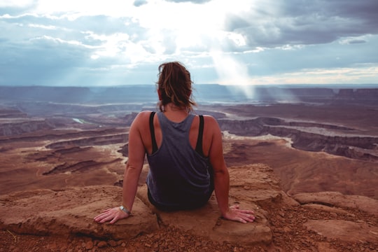 woman sitting on cliff at daytime in Canyonlands National Park United States