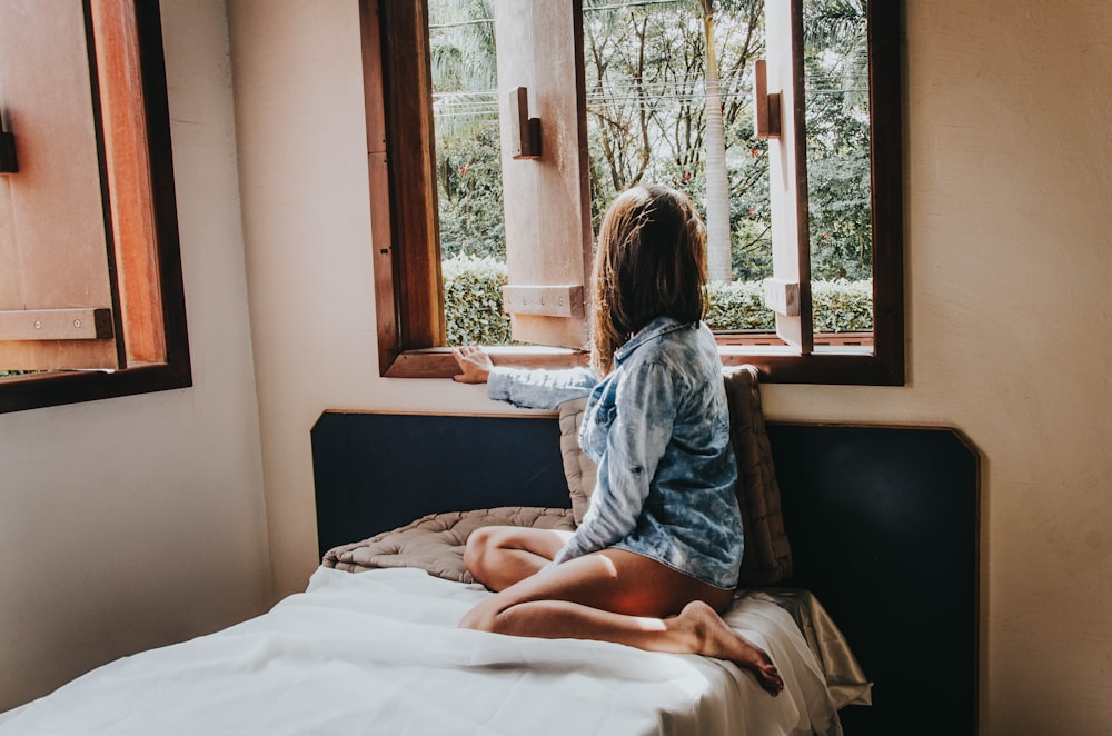 Frau sitzt auf dem Bett und schaut aus dem Fenster