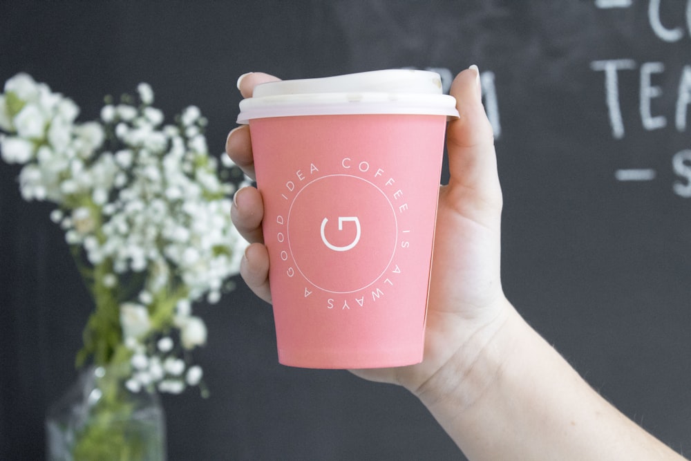 Persona sosteniendo una taza de café desechable rosa y blanca