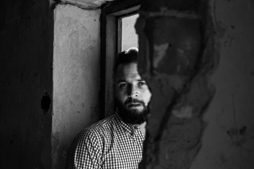 grayscale photography of man leaning against door frame