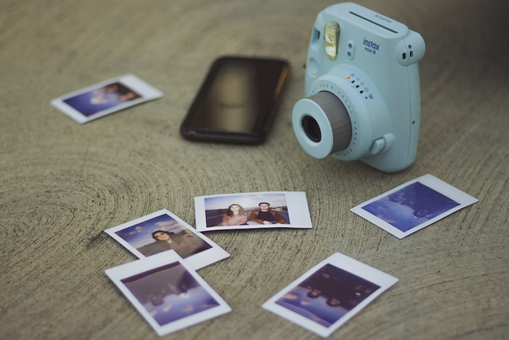 mini câmera Fujifilm Instax branca ao lado de fotos impressas