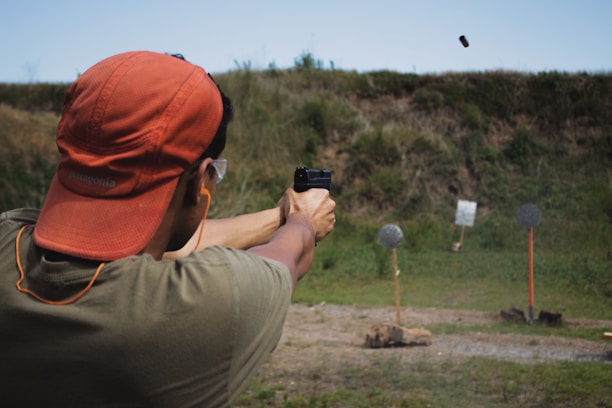 man in brown t-shirt and red knit cap shooting a pistol he is carrying